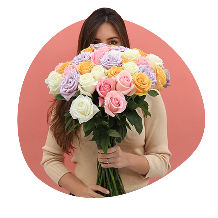 Woman in beige sweater holding hand-tied bouquet of multicolored roses in pink, yellow, purple and white
