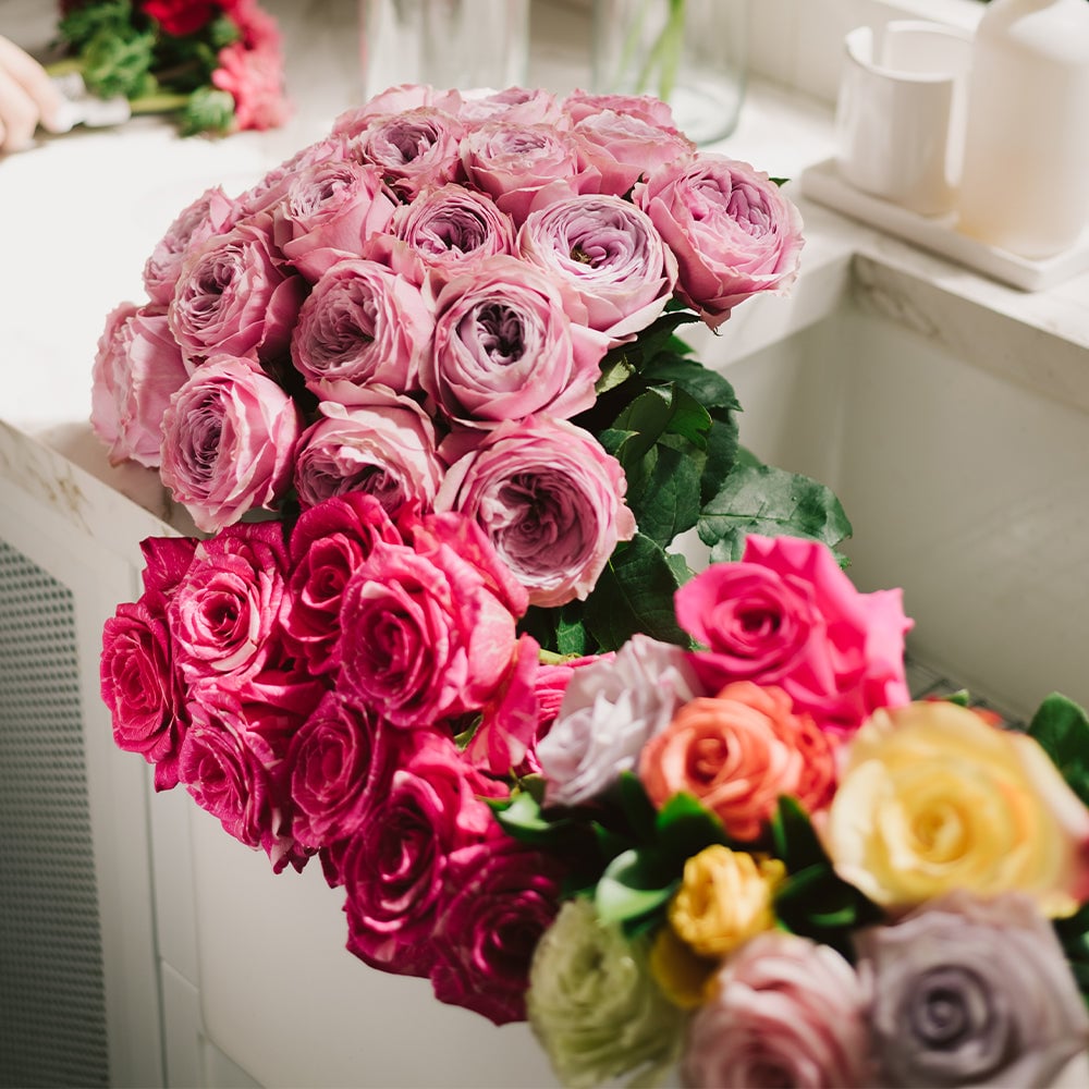 Pink and magenta roses with greenery arranged in a white vase on a marble table