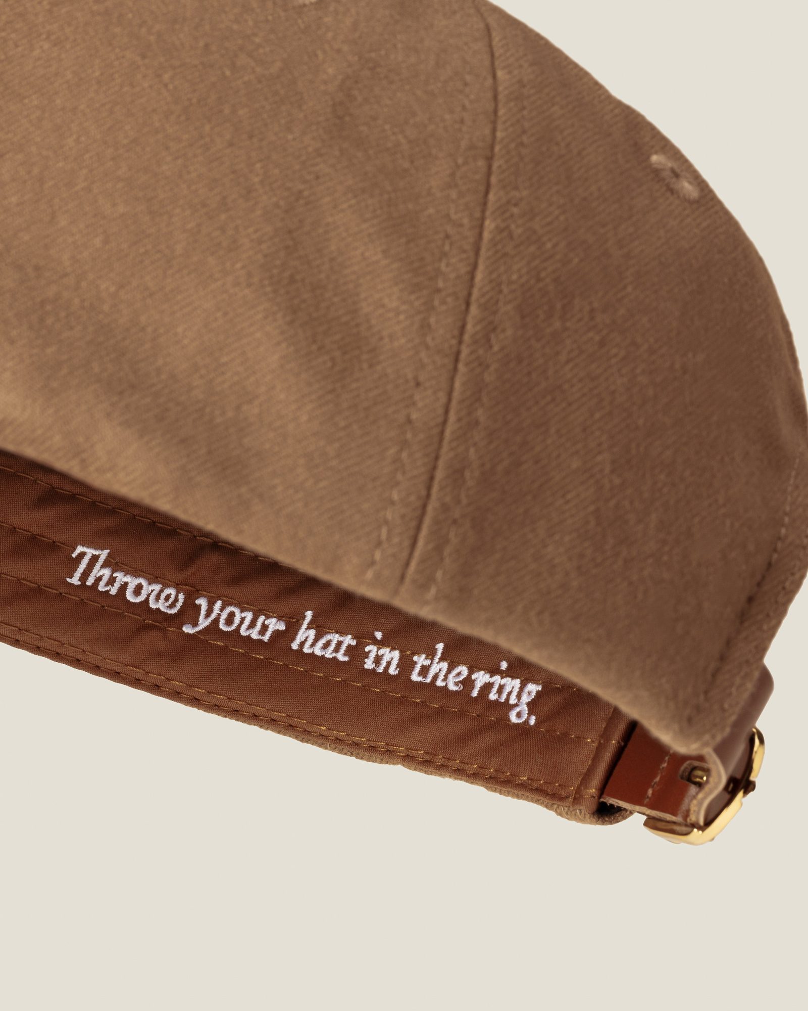 Tan baseball cap with brown strap and 'Throw your hat in the ring' text embroidered on back
