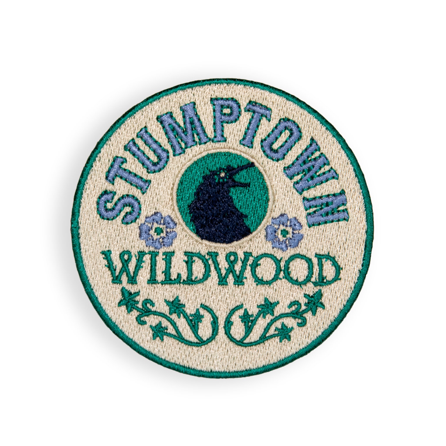 Circular embroidered patch with teal and navy colors featuring Stumptown Wildwood branding and eye symbol