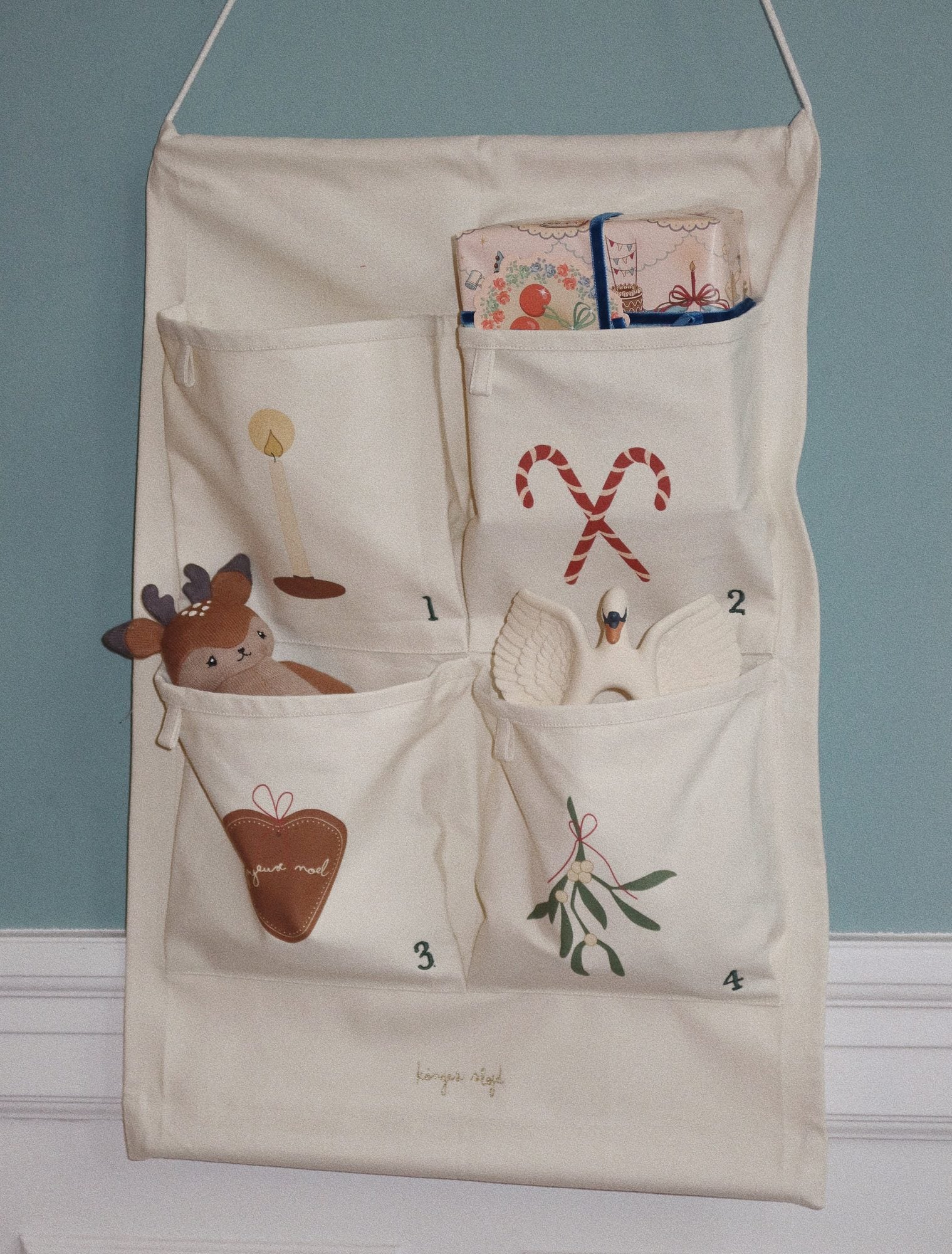 Cream canvas hanging organizer with numbered pockets containing embroidered designs including a reindeer, candy canes, heart, and mistletoe on blue background
