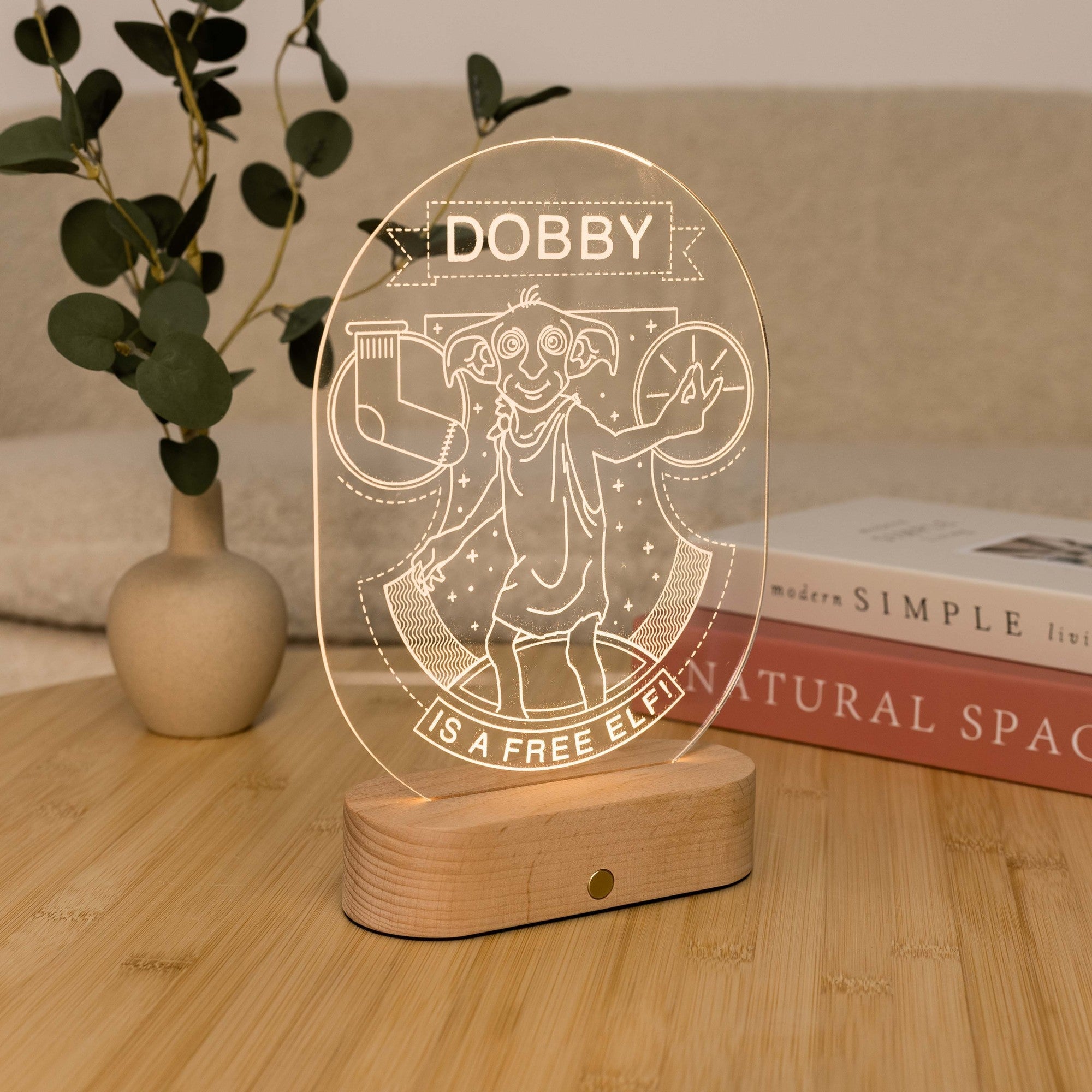 Dobby elf acrylic light-up display on wooden base next to potted plant and books on desk