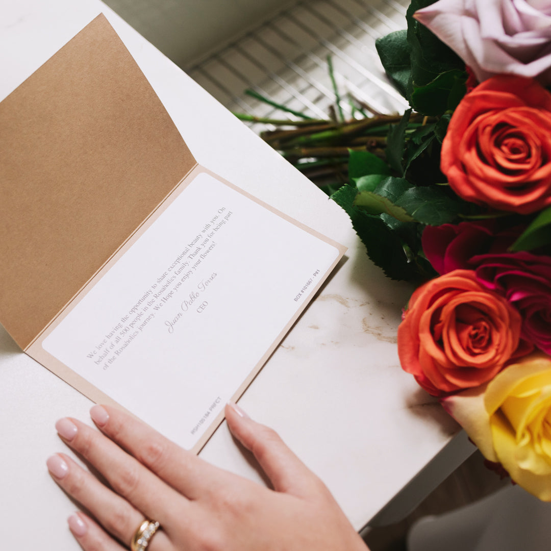 Hands holding an open greeting card with colorful roses including red, orange, and yellow blooms