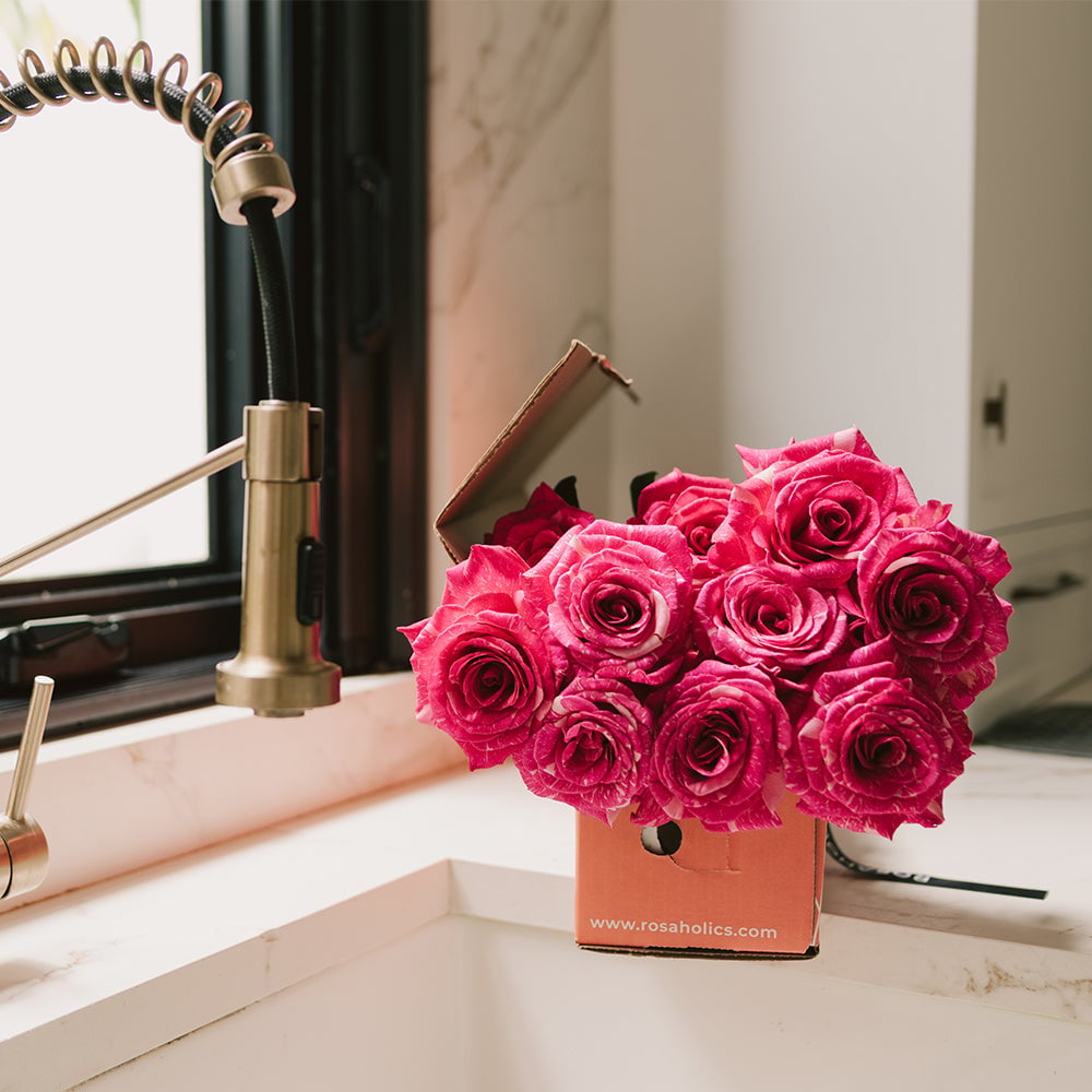 Bright magenta roses in a cardboard box next to a desk lamp and mirror