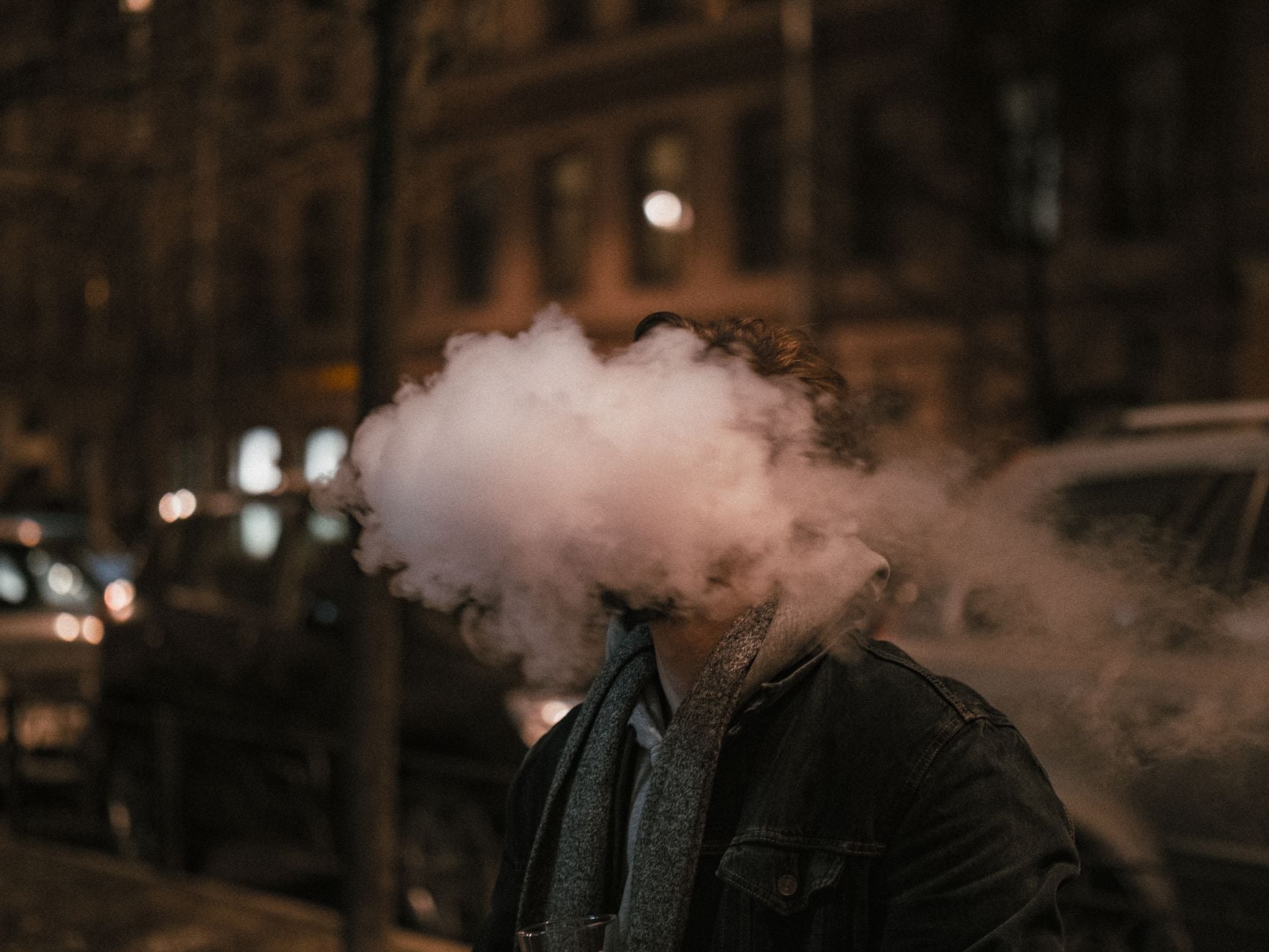 Man exhaling large cloud of vapor on urban street at night