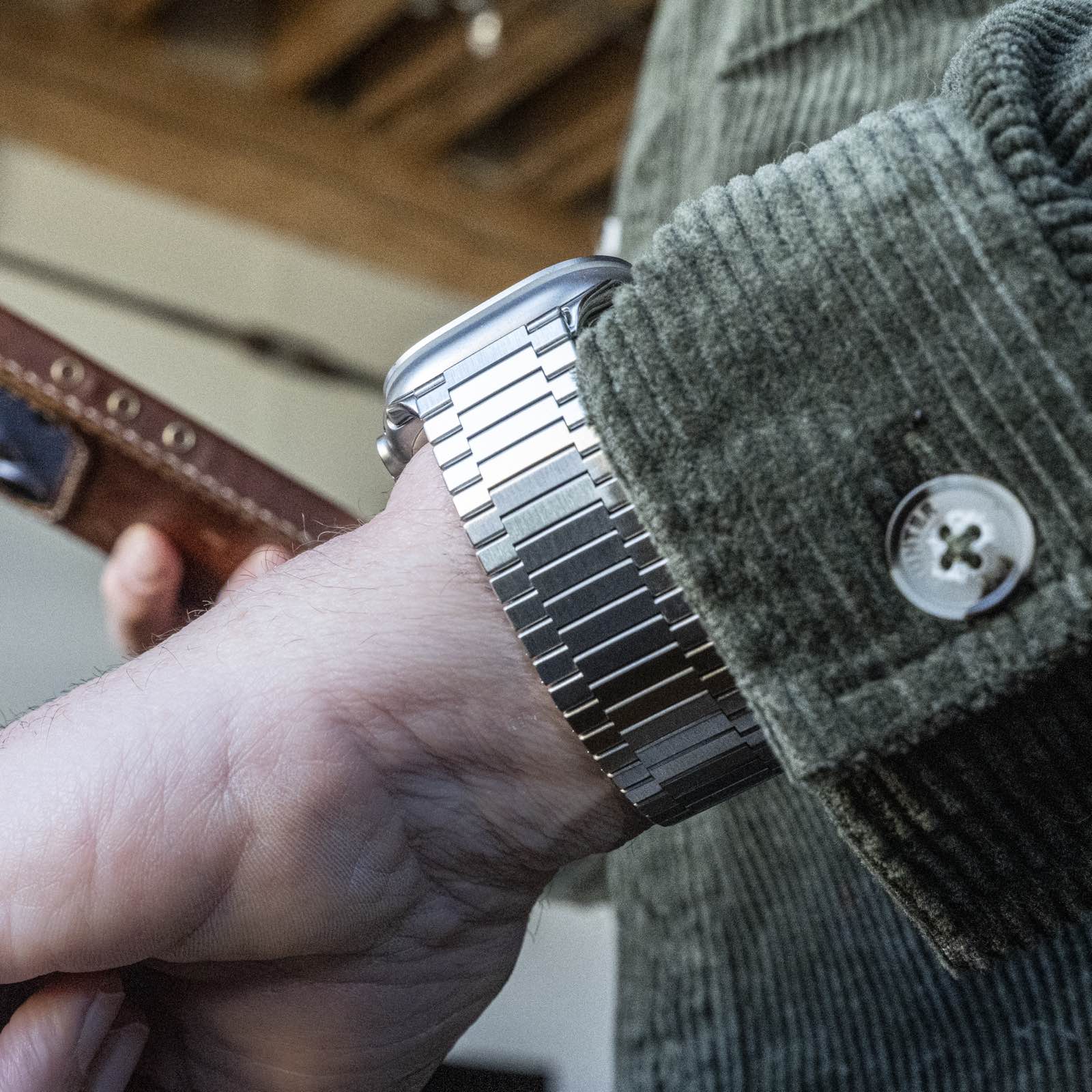 Silver metal link watch band on person's wrist with green sweater and cuff button