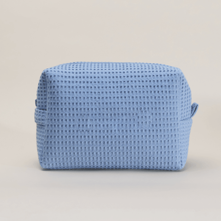 Light blue waffle weave cosmetic bag with small handles on beige background