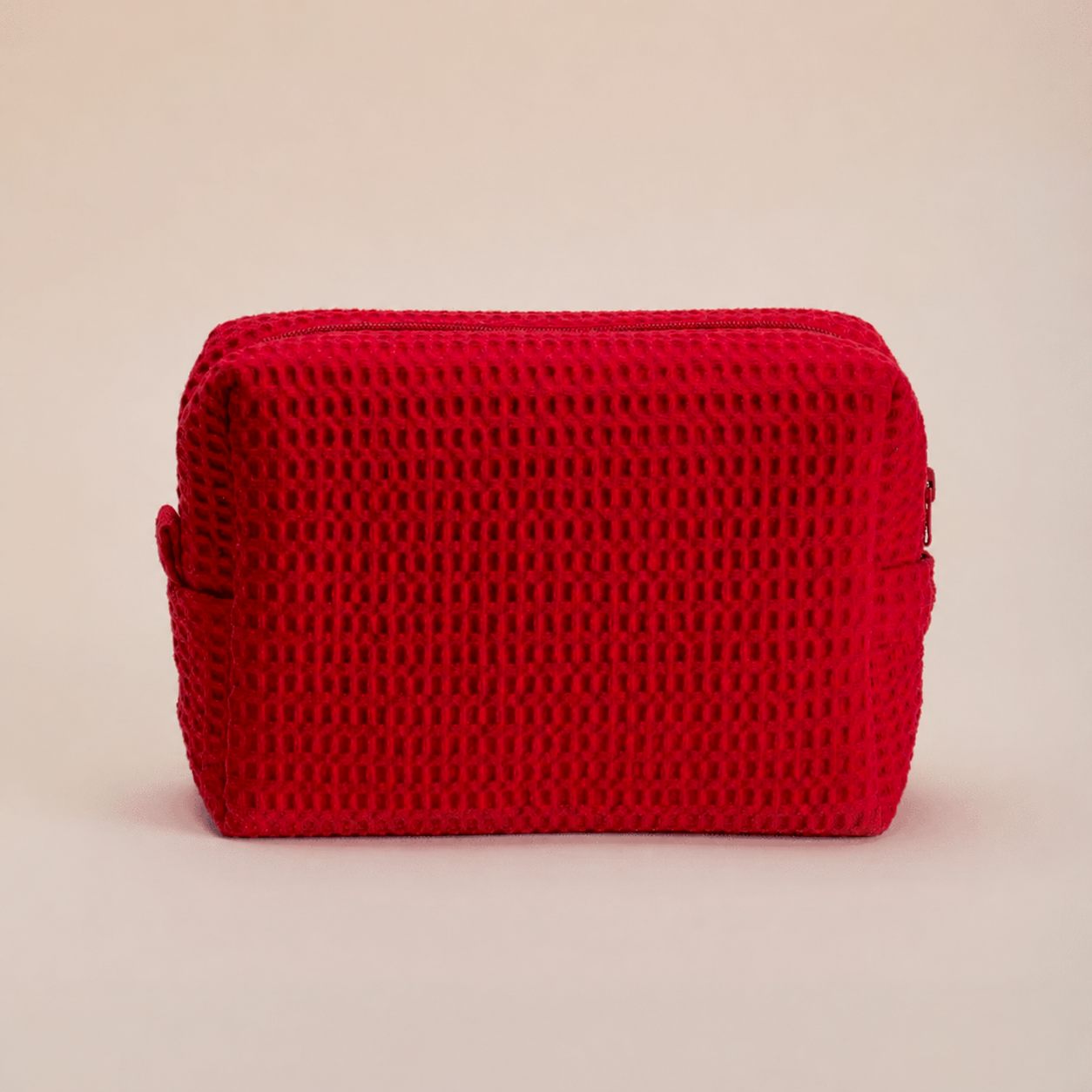 Bright red waffle texture toiletry bag with handles on neutral backdrop