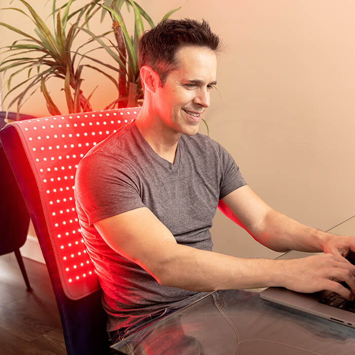 Man sitting at desk using red light therapy pad on back and shoulder