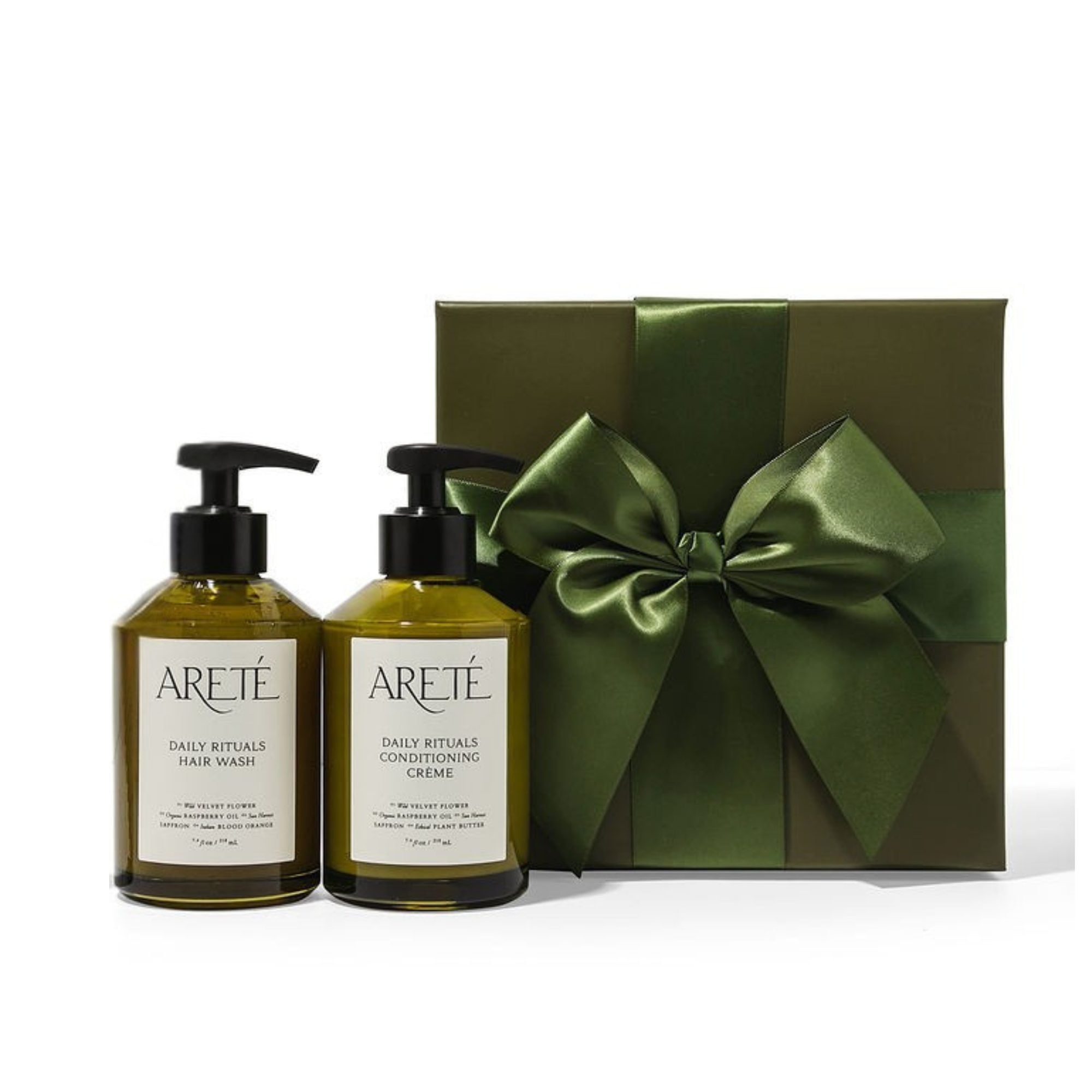 Two green-labeled hair care bottles with black pump dispensers displayed in front of an olive gift box with matching green satin bow