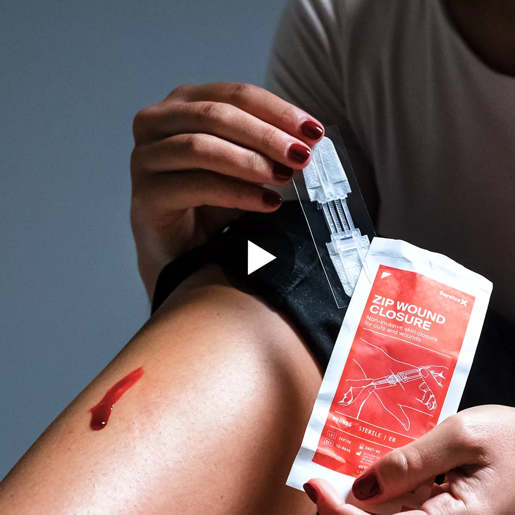 Person's hands holding transparent wound closure strips and red product packaging against blue background
