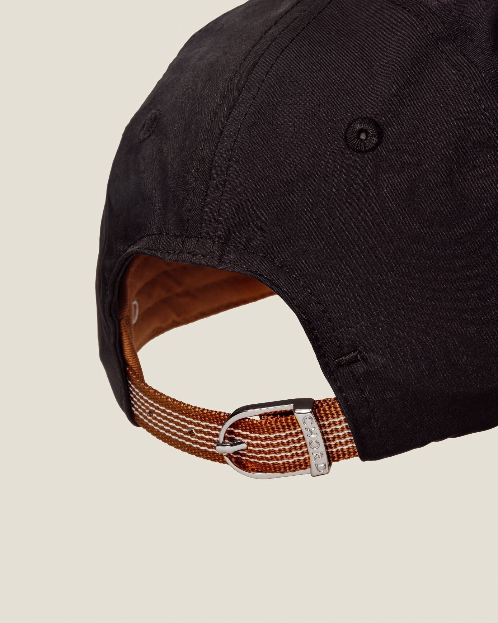 Back view of black baseball cap showing brown fabric strap with metal adjustment buckle