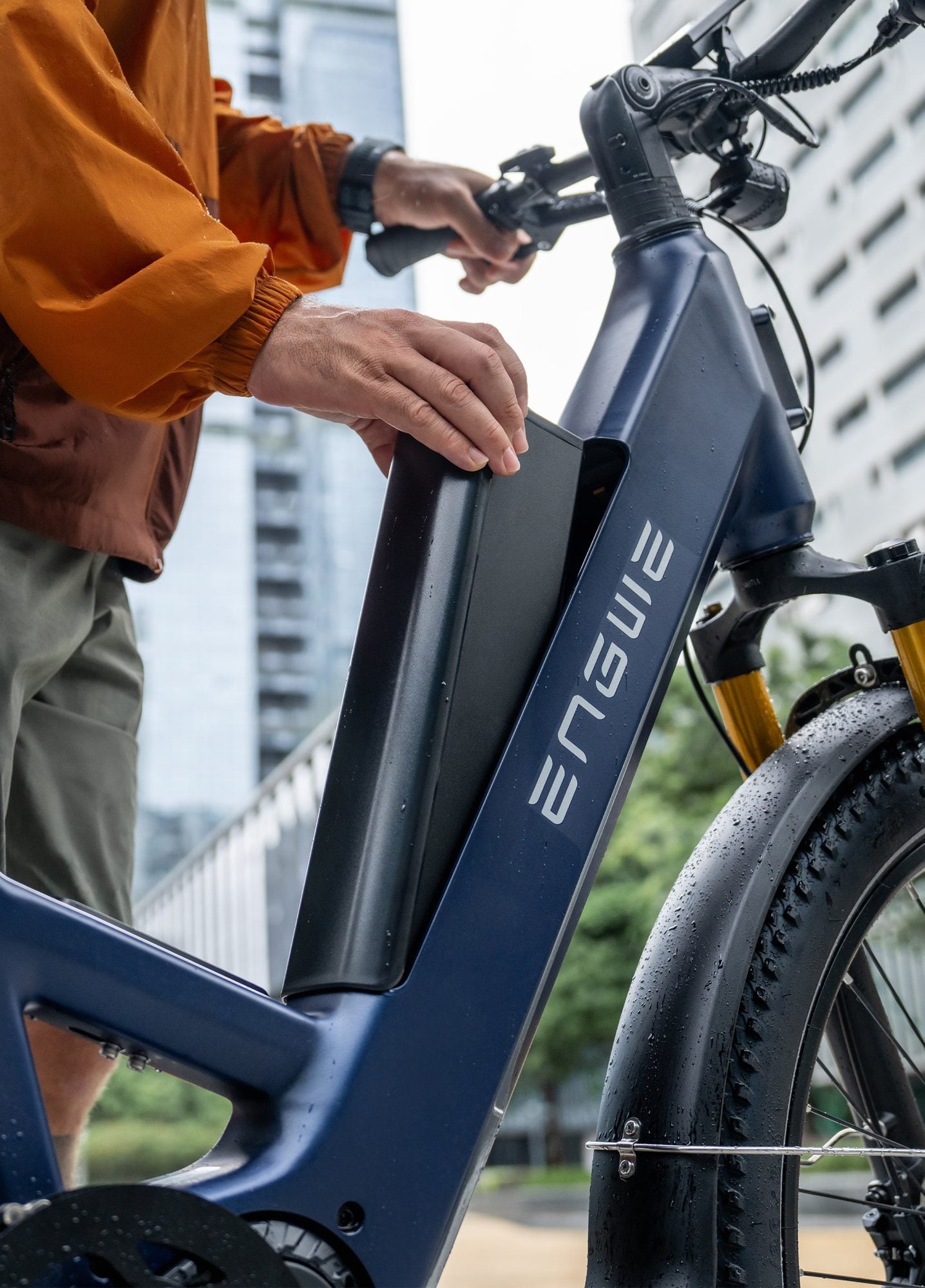 Close-up of a person's hand on the frame of a blue electric bike in an urban setting