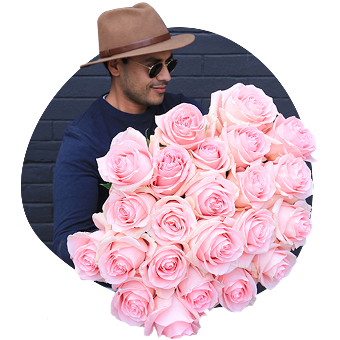Man in navy shirt and brown fedora hat holding large round bouquet of light pink roses