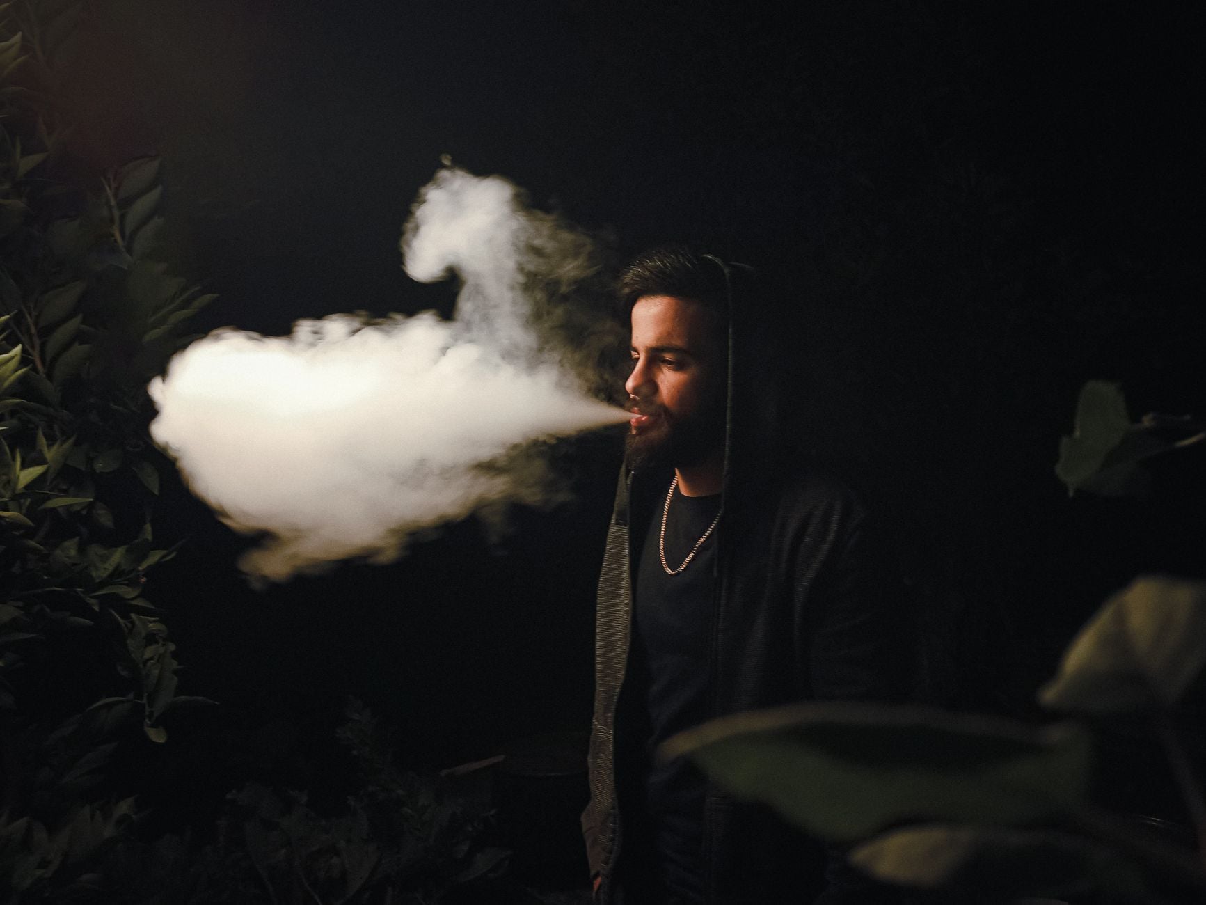 Man vaping outdoors at night with white vapor cloud visible against dark background