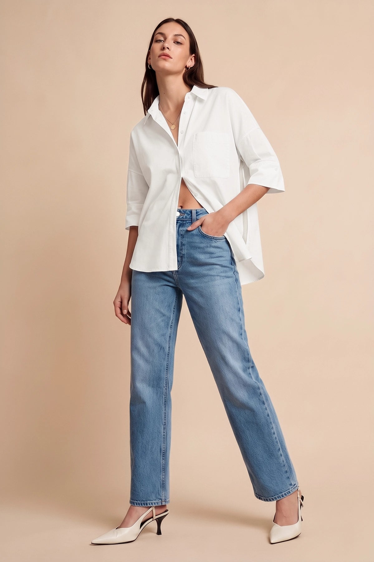 Woman in oversized white button-up shirt tied at waist with blue jeans and white heels