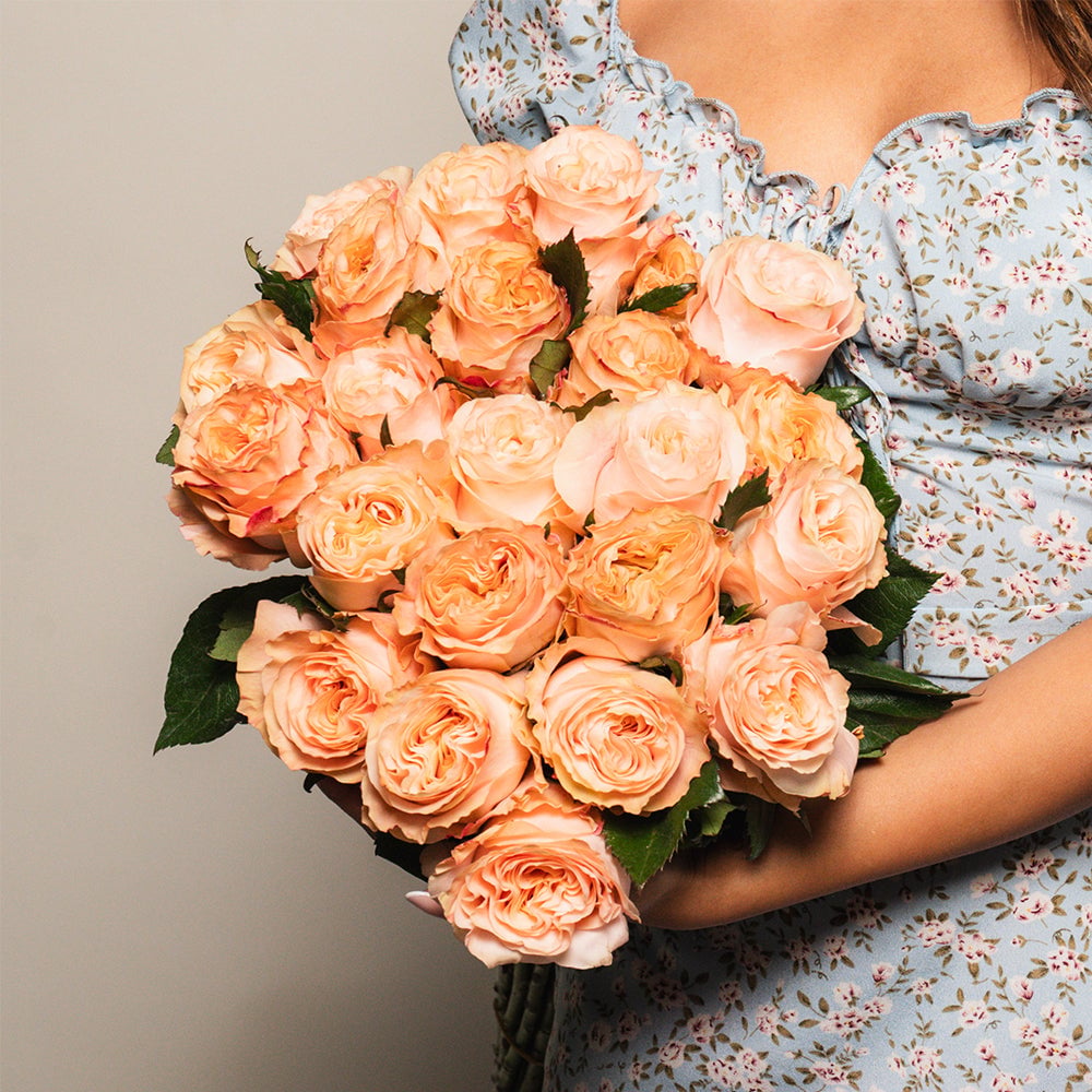 Woman in floral dress holding a bouquet of peachy-orange garden roses with full, layered petals