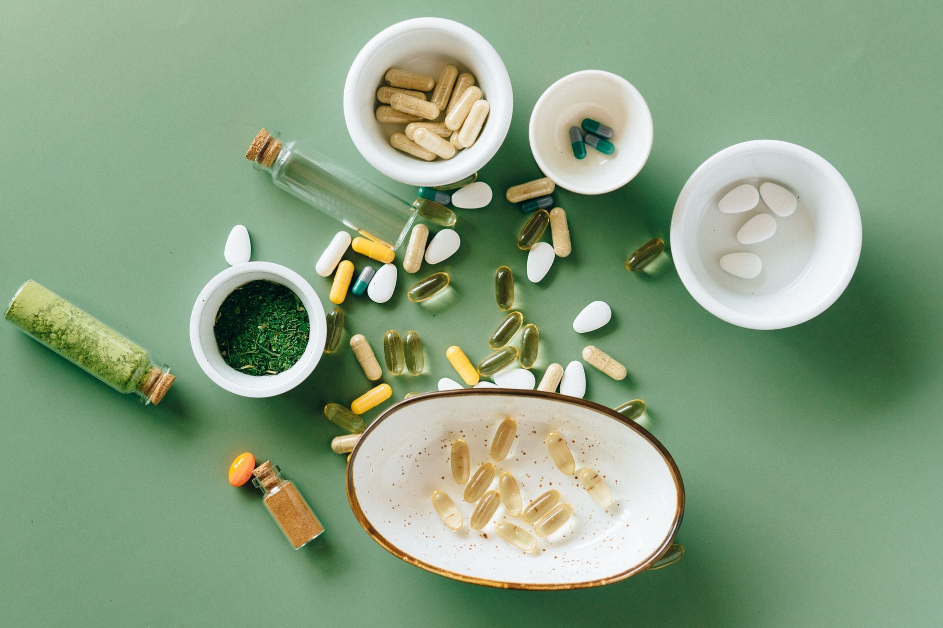 Various dietary supplements including capsules, tablets, and powders arranged in white bowls on a green background